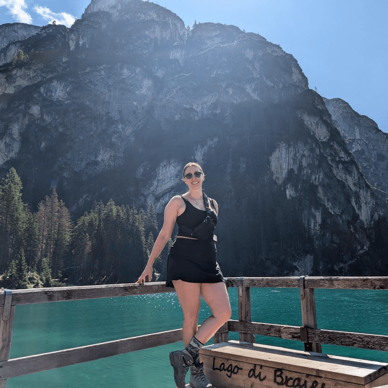 Kelly smiling on a wooden dock at Lago di Braies in the Dolomites, with turquoise water and mountains behind her